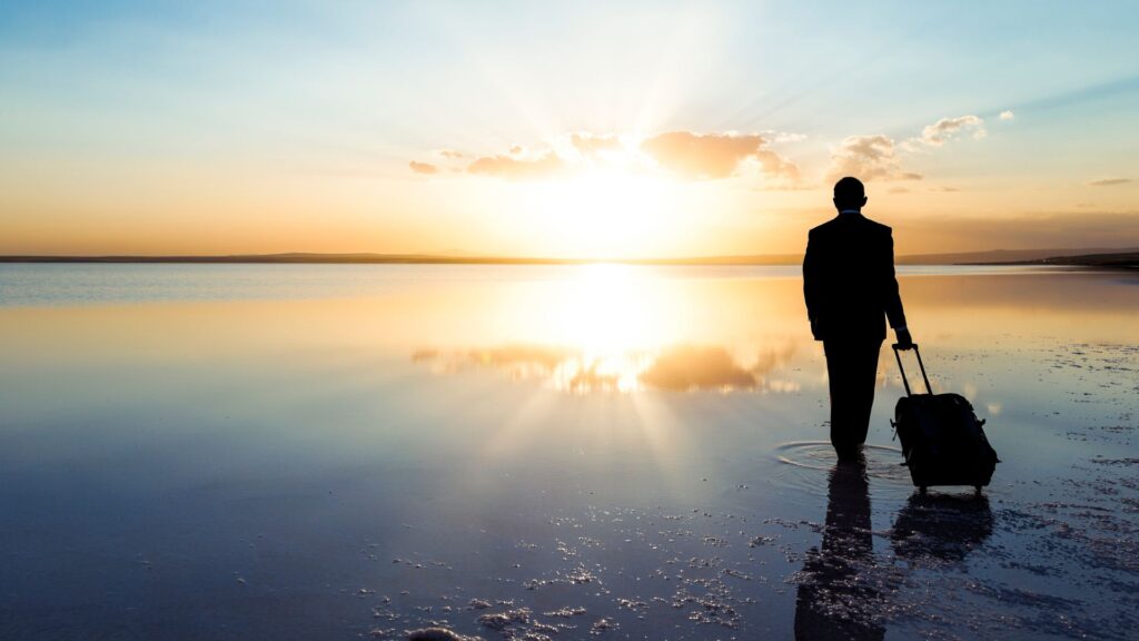 Candidate Journey: Mann geht im Watt mit Rollkoffer in den Sonnenuntergang